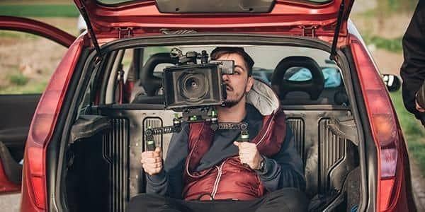 Behind scene improvisation. Cameraman from trunk of car shooting film